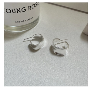 Macro shot of silver matte irregular C-shaped hoop earrings with industrial finish