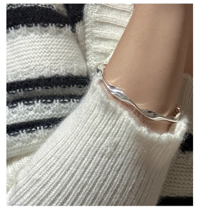Close-up of a wavy twisted silver bangle worn on a wrist over a textured knit sweater