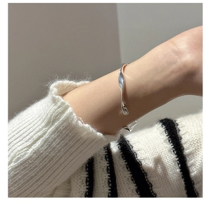 Polished S925 sterling silver twisted wave bangle worn on a model's wrist with a white sweater