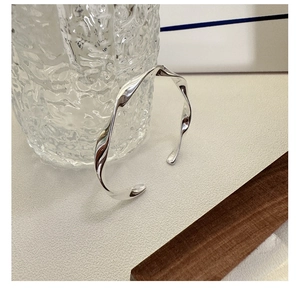 Macro detail of silver S925 twisted wave bracelet on elegant frosted glass and wood base