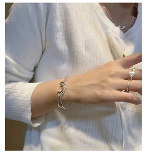 Dettaglio del bracciale S925 argento e anelli stile liquido su maglia bianca