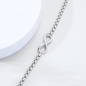 Minimalist silver infinity symbol box chain bracelet on a clean white geometric stand