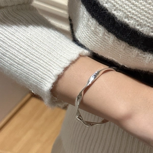 Elegant S925 sterling silver twisted wave bracelet on wrist with striped knitwear