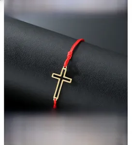 Macro shot of red braided rope bracelet featuring a gold cross charm with black inlay