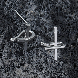 Polished silver stainless steel cross earrings for men on black volcanic rock background