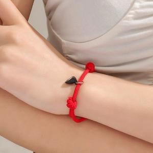 Adjustable woven red rope bracelet featuring a magnetic black heart pendant for couples