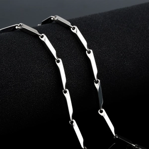 Collier chaîne géométrique argentée à longs maillons sur un socle noir minimaliste