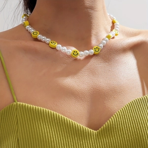 Détail du collier de perles blanches avec des breloques smiley jaunes au cou