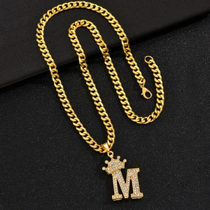 Macro detail of gold-plated Cuban link necklace with iced out crown letter M pendant