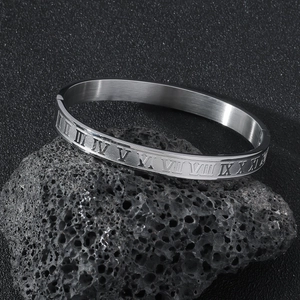 Brushed stainless steel bangle featuring Roman numeral engravings on a dark volcanic rock