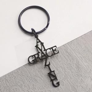 Porte-clés croix Amazing Grace en métal noir mat sur un fond en cuir texturé gris