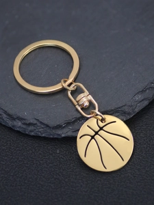 Close-up of a polished gold basketball keychain pendant on a dark slate background
