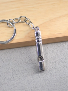 Close-up of polished silver whistle keychain with textured cylindrical body and metal ring