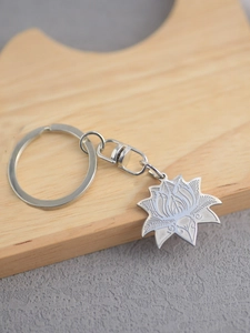 Detailed close-up of a silver stainless steel lotus pendant keychain on a wooden surface