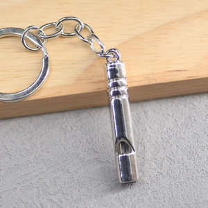 Polished silver metal whistle keychain on wooden surface with industrial link chain