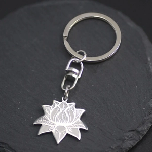 Stainless steel lotus flower keychain with etched details on a dark slate background