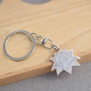 Polished stainless steel lotus flower keychain on a wooden stand with intricate engraving