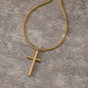 Detailed close-up of a polished gold cross pendant with a tubular design on a box chain