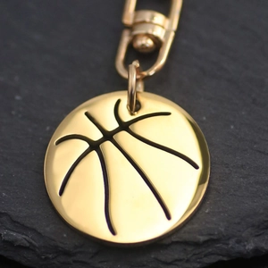 Polished gold basketball pendant keychain with lobster clasp on natural stone background