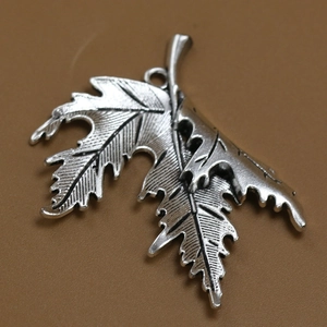 Silver maple leaf pendant necklace with detailed vintage textures on a brown background
