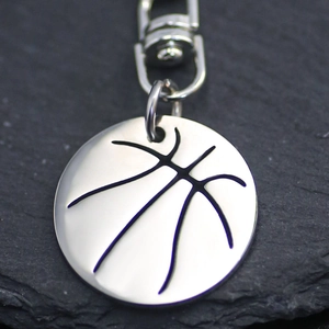 Silver basketball keychain pendant with metallic lobster clasp on dark rock background