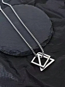 Close-up of minimalist geometric double triangle pendant on a fine box chain over dark stone