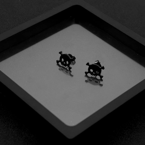 Macro shot of gothic black skull and crossbones stud earrings in a dark punk aesthetic