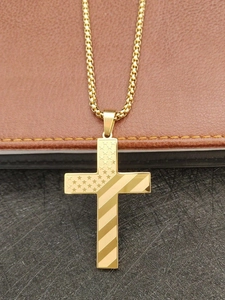 Détail macro du pendentif croix en acier doré avec motif d'étoiles et de rayures US