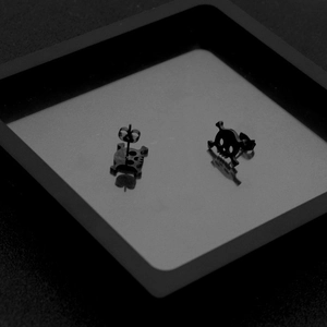 Close-up of black punk skull stud earrings with polished finish on a minimalist display