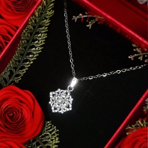 Gros plan d'un pendentif flocon avec perle et zircons sur fond de boîte cadeau roses rouges