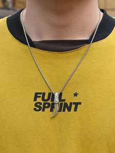 Gros plan d'une chaîne argentée avec pendentif dent de loup sur un sweat à capuche