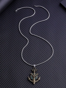 Détail du pendentif ancre et gouvernail vintage sur une chaîne à mailles carrées argentée