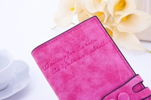 Gros plan sur un portefeuille rose mat avec applique florale et texte gaufré