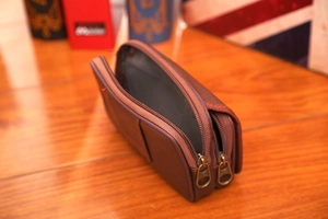 Detail of dark brown leather waist bag featuring double zippers and orange stitching