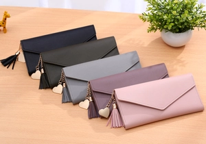 Close-up of five colorful envelope wallets with heart pendants and tassels on wood