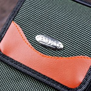 Macro shot of durable green Oxford fabric with orange leather trim and metal logo plate