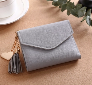 Short grey litchi grain leather wallet with heart pendant and tassel on beige background