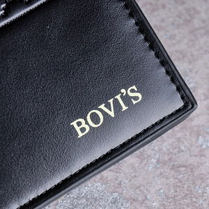 Macro shot of black leather wallet texture with gold engraved logo on stone surface