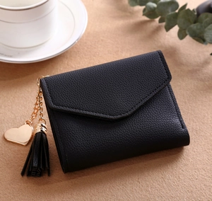 Detail view of black lychee leather short wallet with gold heart pendant and tassel accent