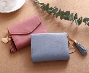 Detail of lychee textured wallets with tassel pendant and golden heart charm on soft brown surface