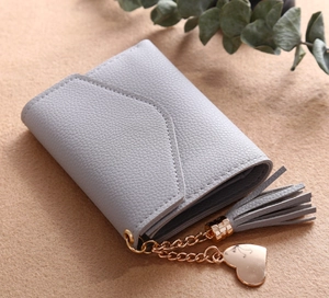 Detail of short tri-fold wallet featuring litchi texture leather and tassel pendant