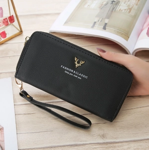 Detail of black pebbled leather wallet with golden deer ornament and hand strap on wood