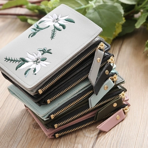 Close-up of floral embroidery on leather wallets with golden metal zippers on a wooden table