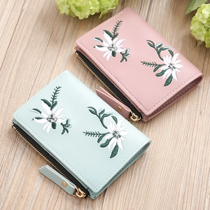 Close-up of floral embroidery on small pink and green leather zipper wallets