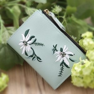 Detail of mint green zippered wallet with delicate floral embroidery on litchi grain leather