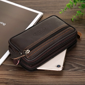 Detail of dark brown leather phone bag with three zippers and orange stitching on wood
