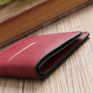 Macro detail of red lychee grain leather wallet with white stitching and black oil edge