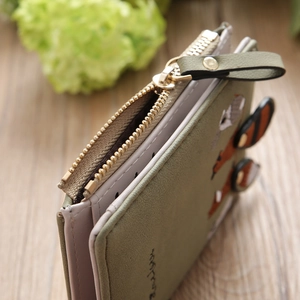 Detailed shot of olive green bifold wallet featuring animal embroidery and golden zipper