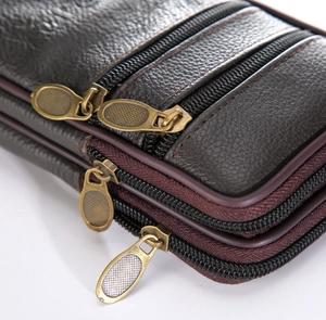 Detail of dark brown leather waist bag featuring multi-layer zippers and grain texture