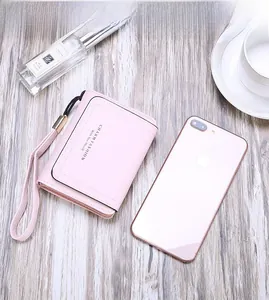 Close-up of pink PU leather tri-fold wallet with wristlet on light wooden background